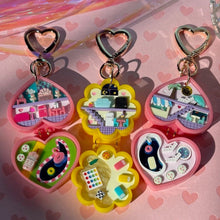 Load image into Gallery viewer, A collection of colorful bag charms designed to look like pockets with various items inside, attached to heart-shaped key clasps.